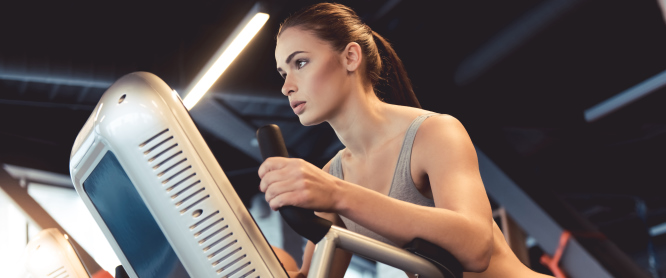 Attractive young woman is working out on an elliptical trainer in gym